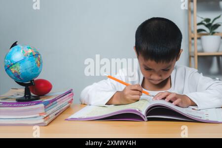 Bildungskonzept, trauriger müder, frustrierter Junge, der mit vielen Büchern am Tisch sitzt, gelangweilter und müder Junge, der auf dem Schreibtisch in seinem Zimmer Hausaufgaben macht, Dif lernt Stockfoto