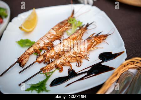 Ein weißer Teller hält gegrillte Garnelenspieße, getränkt mit Balsamico-Glasur und einem Zitronenkeil. Familienurlaubskonzept Stockfoto