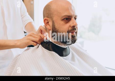 In einem Friseurladen gibt ein lateinamerikanischer Mann einem kahlköpfigen Bärtigen im Friseursalon einen Haarschnitt Stockfoto