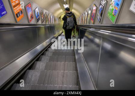 Ein Mann mit einem Rucksack auf einer Rolltreppe, der in Richtung einer Londoner U-Bahn-Linie fährt, leer, Silber, isoliert Stockfoto