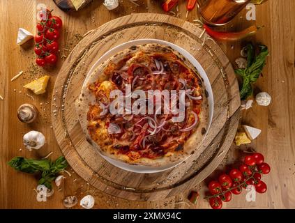 Appetitliche Pizza mit Zwiebeln, Tomaten, Schinken und Peperoni auf einem rustikalen Holztisch, Blick von oben Stockfoto