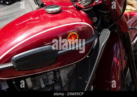 Nahaufnahme eines alten roten sowjetischen Ural-Motorrads mit Emblem und Details, die das klassische Design und die mechanischen Komponenten hervorheben. Stockfoto