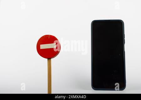 Neben einem Smartphone befindet sich auf einem sauberen weißen Hintergrund ein Holzspielzeug mit der Aufschrift „kein Zutritt“. Die Einrichtung betont den Kontrast zwischen alten und neuen Communi Stockfoto