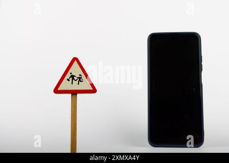 Neben einem Smartphone befindet sich ein Warnschild mit der Aufschrift „WARNUNGEN KINDER“ auf einem sauberen weißen Hintergrund, das Sicherheit und Technologie hervorhebt Stockfoto