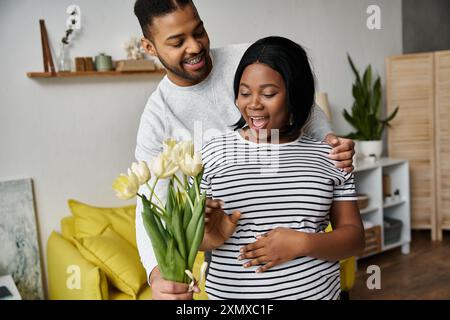 Ein Mann überrascht seine schwangere Frau zu Hause mit Blumen. Stockfoto