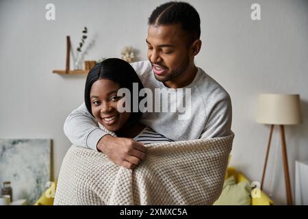 Ein liebevolles Paar kuschelt sich unter einer Decke in ihrem Haus, während der Mann seinen Partner in der Nähe hält. Stockfoto