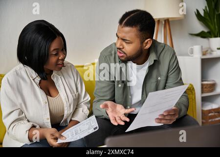 Ein junges afroamerikanisches Paar sitzt auf einer Couch, überprüft Rechnungen und diskutiert Finanzen. Stockfoto