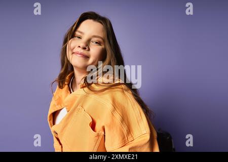 Eine selbstbewusste junge Frau strahlt vor Freude und zeigt stilvolle Freizeitkleidung vor einem leuchtend violetten Hintergrund. Stockfoto