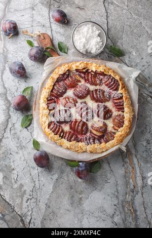 Hausgemachter Pflaumengalette-Kuchen mit Mandeln und Puderzucker in Nahaufnahme auf einem Holzbrett auf dem Tisch. Vertikale Draufsicht von oben Stockfoto