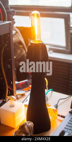 Art Object Lampe mit einer leuchtenden Glühlampe in Form einer menschlichen Hand, die auf einem 3D-Drucker gedruckt wird. Modellprototyp menschlicher Hand, gedruckt auf 3D-Drucker aus geschmolzenem Kunststoff, der auf dem Tisch steht. Stockfoto