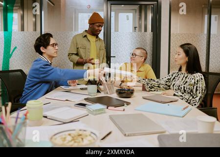 Gruppe von jungen ethnisch unterschiedlichen Menschen, die legere Kleidung tragen und während der Besprechung im Sitzungsraum gemeinsam an Projekten arbeiten Stockfoto