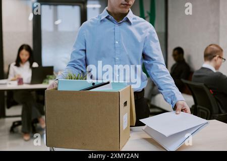 Mittelgroße Aufnahme eines neuen Mitarbeiters, der am Schreibtisch steht und Dokumente und Dinge im Büro aus dem Karton nimmt Stockfoto