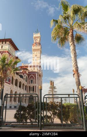 Alexandria, Ägypten - 13. Dezember 2018: Außenansicht des Montazah-Palastes an einem sonnigen Tag, vertikales Foto mit Stahlzaun und Palme im Vordergrund Stockfoto