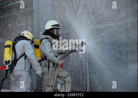 Retter in Gummischutzanzügen und in sich geschlossenen Atemgeräten von Drager, die Pflanzengebiet mit Spritze bewässern. Training für Rettungsteams Stockfoto