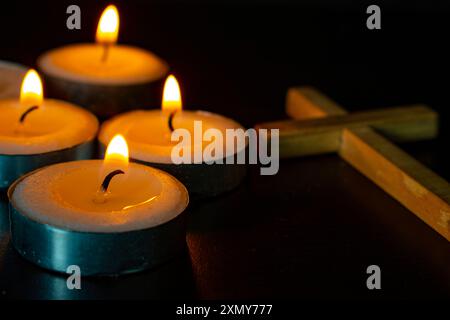 Kerzen mit dem Heiligen Kreuz auf dunklem Hintergrund. Christentum-Konzept. Stockfoto