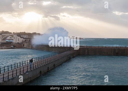 Alexandria, Ägypten - 19. Dezember 2018: Fischer ist an einem stürmischen Tag auf einem Pier, eine große Welle bricht an der Ufermauer im Hintergrund Stockfoto