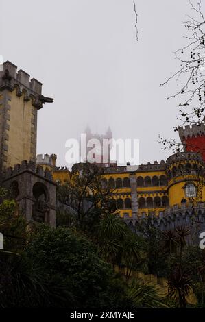 Die ikonischen Gebäude der Pena Palace, während der berühmte rote Uhrturm an einem nebeligen Tag einen schweren Nebel durchstößt Stockfoto