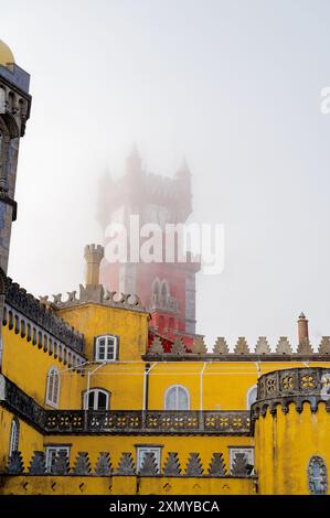 Die ikonischen Gebäude der Pena Palace, während der berühmte rote Uhrturm an einem nebeligen Tag einen schweren Nebel durchstößt Stockfoto