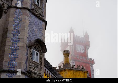 Die ikonischen Gebäude der Pena Palace, während der berühmte rote Uhrturm an einem nebeligen Tag einen schweren Nebel durchstößt Stockfoto