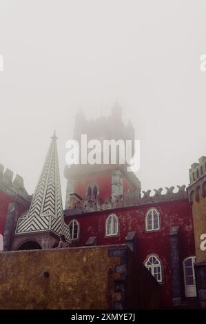 Die ikonischen Gebäude der Pena Palace, während der berühmte rote Uhrturm an einem nebeligen Tag einen schweren Nebel durchstößt Stockfoto