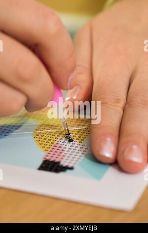 Eine Nahaufnahme einer Hand, die Kristalle auf einer Leinwand für ein Diamantmalprojekt platziert. Diamantmosaik Stockfoto