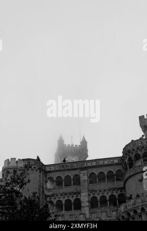 Die ikonischen Gebäude der Pena Palace, während der berühmte rote Uhrturm an einem nebeligen Tag einen schweren Nebel durchstößt Stockfoto