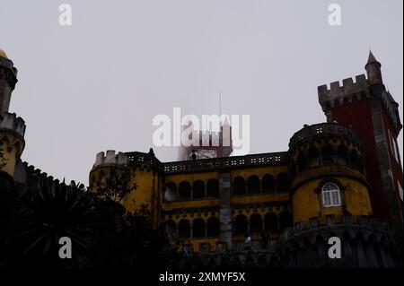 Die ikonischen Gebäude der Pena Palace, während der berühmte rote Uhrturm an einem nebeligen Tag einen schweren Nebel durchstößt Stockfoto