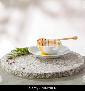Honig mit Honiglöffel in weißer Schüssel auf einem Tisch. Weiße Wand mit natürlichem Bokeh-Hintergrund und Kopierraum für Produkte. Stockfoto