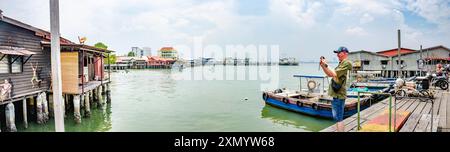 Panoramablick von Chew Jetty, George Town, Penang, Malaysia mit Booten, die an der hölzernen Promenade verankert sind und ein Mann fotografiert Stockfoto