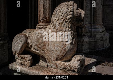 Mittelalterlicher Löwe trägt Säule am Südostportal zur Kathedrale in Trient, Italien, der Basilika-Duomo di San Vigil. Auf der rechten Seite dieses Bildes befinden sich zwei von drei aus Marmor gefertigten Sitzfiguren, die sich am Fuß einer anderen Säule befinden. Die drei Figuren sollen die Söhne des Mannes darstellen, der Anfang der 1200er Jahre den Wiederaufbau der Kathedrale im romanisch-lombardischen Stil, Maestro Adama d’Arogno, gemeistert hat. Stockfoto