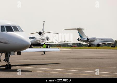 Die Bodencrew manövriert einen Falcon 8X in Position, mit einem NetJets Dassault Falcon 2000EX im Vordergrund und einem Bombardier Global 6000 im Rollfeld. Stockfoto