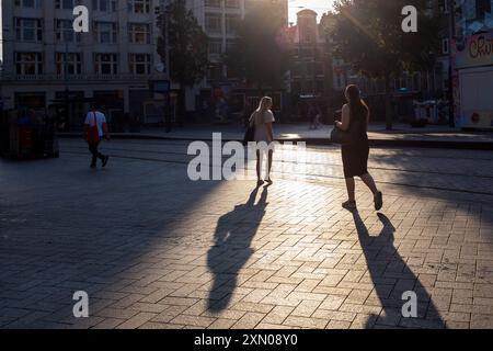 Die Menschen werfen Schatten auf ihrem Morgenspaziergang zur Arbeit in den ruhigen Straßen Amsterdams, Niederlande. Stockfoto