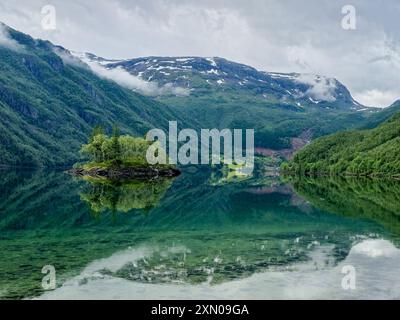 Ein ruhiger See spiegelt die umliegenden Berge und das üppige Grün wider und schafft eine perfekte Harmonie der Natur während der Dämmerung. Stockfoto