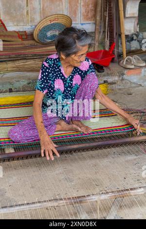 Ältere vietnamesische Frau webt im Juni Schlafmatten aus getrocknetem und gefärbtem Schilf auf einem Webstuhl im Dorf Tra Nhieu, Quảng Nam, Zentralvietnam, Asien Stockfoto