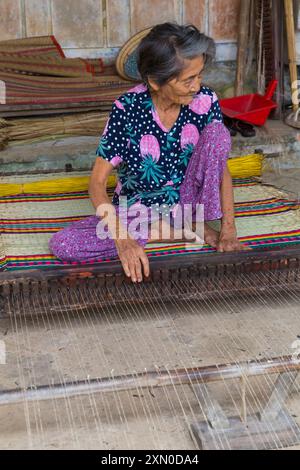 Ältere vietnamesische Frau webt im Juni Schlafmatten aus getrocknetem und gefärbtem Schilf auf einem Webstuhl im Dorf Tra Nhieu, Quảng Nam, Zentralvietnam, Asien Stockfoto