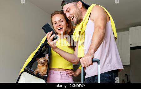 Glückliches junges Paar mit ihrem Lapdog in der Haustiertransporter bei der Buchung von Reisen online über das Handy. Bereit für den Sommerurlaub. Stockfoto