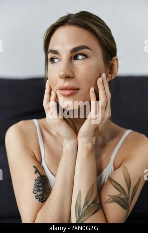 Eine junge Frau mit Vitiligo sitzt in einer modernen Wohnung, während ihre Hände auf ihrem Gesicht liegen, während sie meditiert. Stockfoto