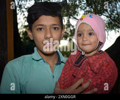 Glücklicher asiatischer Junge, der seine kleine Schwester hält, warme rosa Kleider, selektiver Fokus im Thema Stockfoto