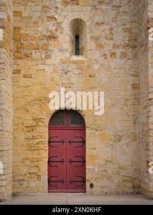 Saintes Maries de la Mer, Frankreich - 9. März 2023: Die Kirche Saintes Maries de la Mer an einem bewölkten Tag im Frühling, rote Tür Les Saintes-Maries-de Stockfoto