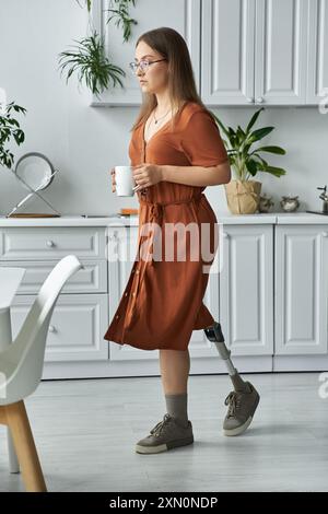 Eine Frau in einem orangefarbenen Kleid geht mit einer Tasse Kaffee in der Hand durch ihre Küche. Stockfoto