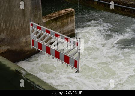 Ein Schutzzaun an der Seite eines offenen Damms mit einer weiß-rot gestreiften Barriere, umgeben von fließendem Wasser. Stockfoto