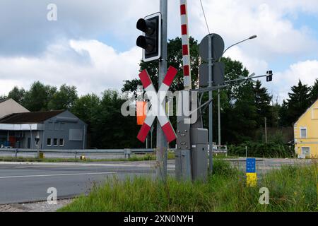 Ein Bahnübergang mit einem Signalsystem, Barrieren und umliegendem Grün in einem Vorstadtviertel während des Tages. Stockfoto