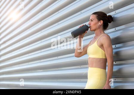 Sportliche Frau, die nach dem Training im Freien Wasser aus der Flasche trinkt Stockfoto