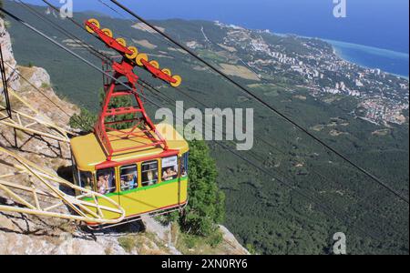 Russland, Krim, August 2015: Das gelbe Fahrerhaus der Seilbahn mit Menschen im Inneren bestiegen den Berg auf der Krim. Blick von oben auf Berge, Wald und Meer Stockfoto