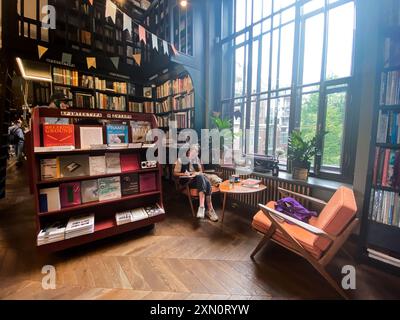 St. Petersburg, Russland, August 2021: Moderne gemütliche Buchhandlung. Die junge Frau sitzt neben dem Fenster auf dem Sessel, liest, schreibt mit einem kleinen flauschigen Hund. Stockfoto