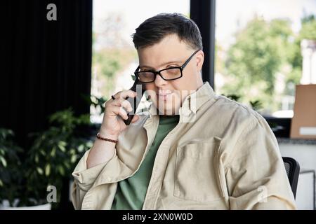 Ein junger Mann mit Down-Syndrom sitzt auf einem Stuhl und spricht mit seinem Telefon. Stockfoto