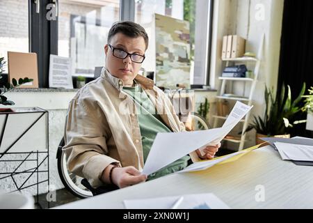 Ein junger Mann mit Down-Syndrom sitzt an seinem Schreibtisch und überprüft Dokumente. Stockfoto