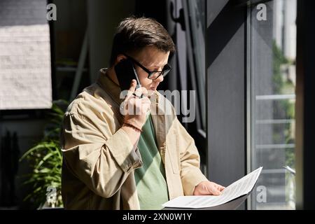 Ein junger Mann mit Down-Syndrom spricht am Telefon, während er sich Notizen ansieht. Stockfoto