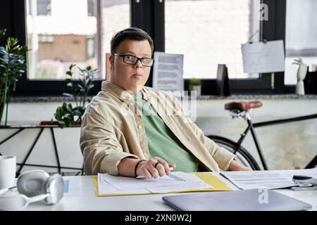 Ein junger Mann mit Down-Syndrom sitzt an einem Schreibtisch und arbeitet an Papierkram. Stockfoto
