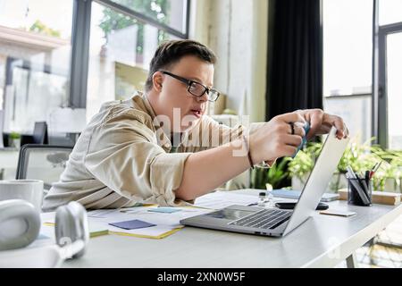 Ein junger Mann mit Down-Syndrom arbeitet an seinem Laptop und konzentriert sich auf seine Aufgabe. Stockfoto